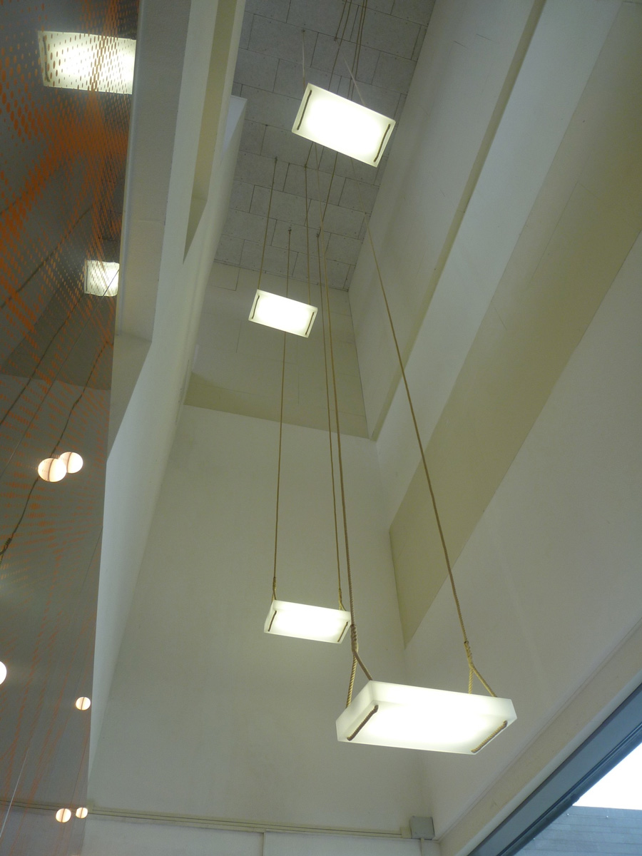 De Schommels zijn lichtobjecten die aan 12 meter lange touwen hangen en daarmee de bijzonder hoge en smalle ruimte benadrukken.